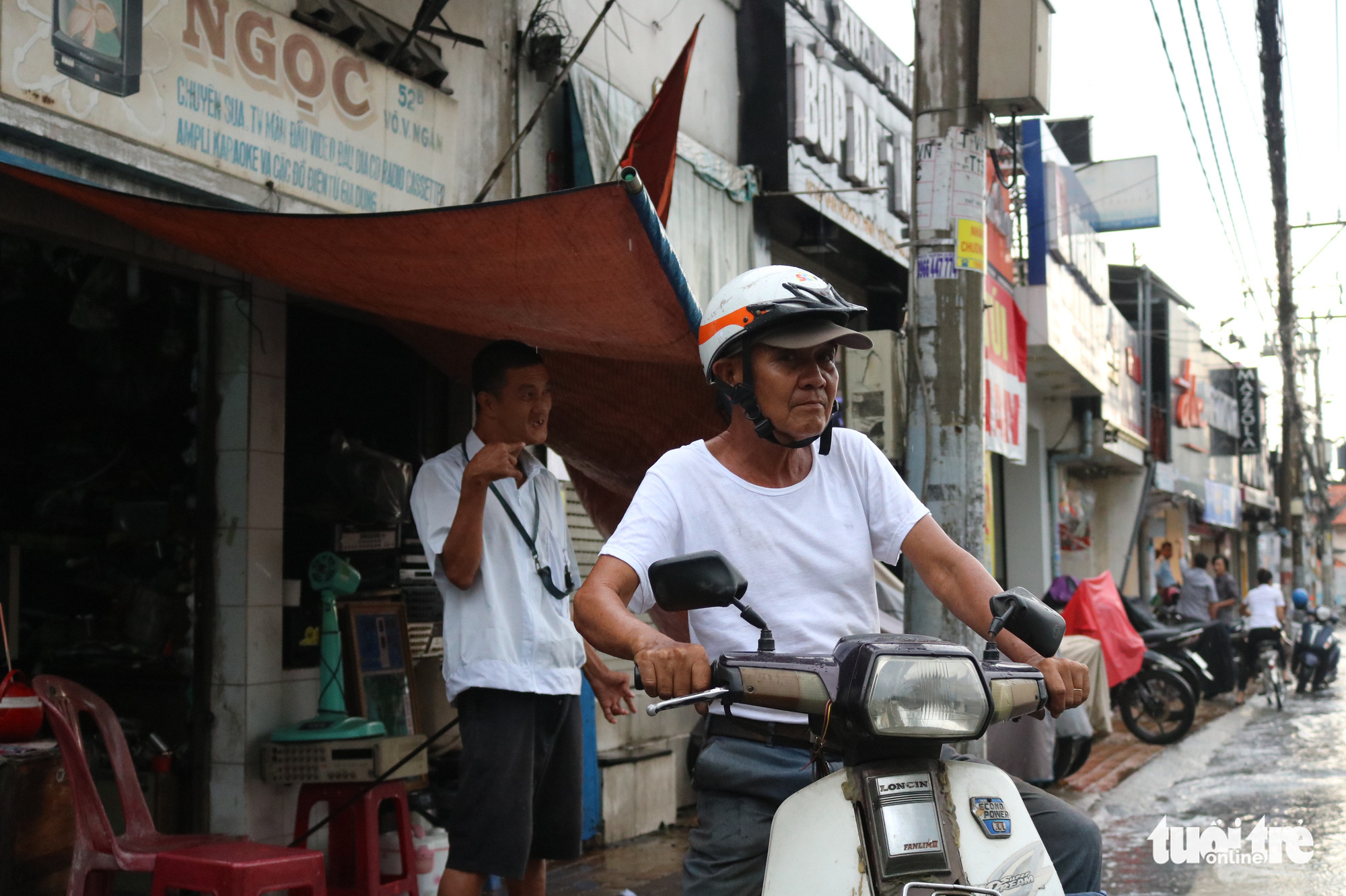 Tran Minh Tri (right) prepares for a motorbike taxi gig, leaving his son Anh Tu taking care of the repair shop on Vo Van Ngan Street in Thu Duc District, Ho Chi Minh City. Photo: Hoang An / Tuoi Tre