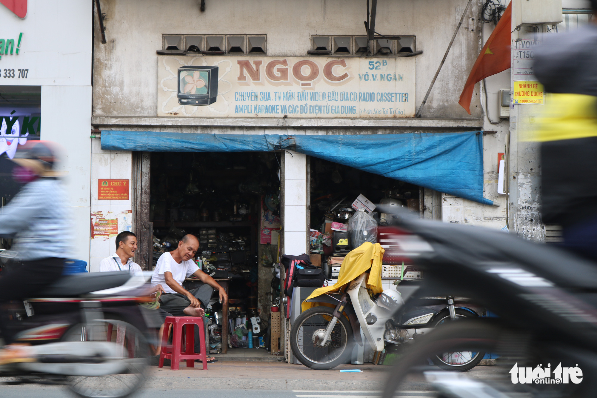 Tran Minh Tri (right) and his son Anh Tu sit in front of their radio repair shop on Vo Van Ngan Street in Thu Duc District, Ho Chi Minh City. Photo: Hoang An / Tuoi Tre