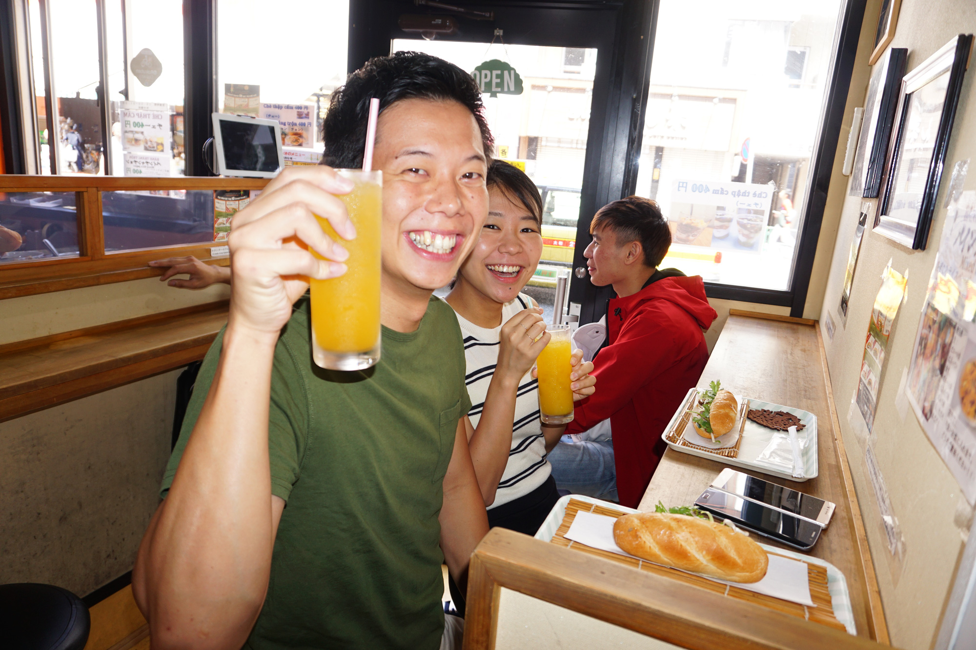 Two Japanese diners hold up their drinks while sitting in front of their loaves of 'banh mi' at a Banh Mi Xin Chao store in Tokyo, Japan. Photo: Cong Nhat / Tuoi Tre
