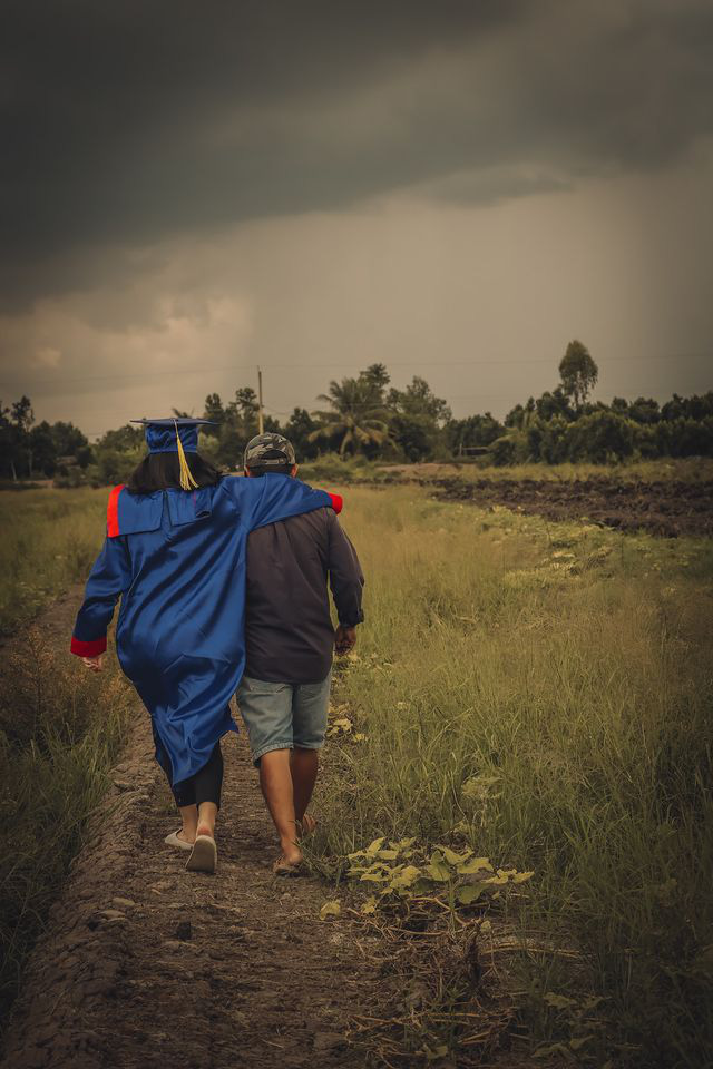 A student in a graduation gown is seen walking next to her father on the rural field. Photo: Pham Van Thong