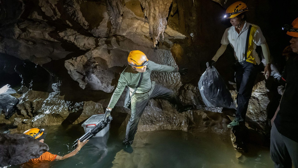 Expedition members pass photography and lighting devices through a stream inside a cave in Quang Binh Province, Vietnam. Photo: Hoang Nhiem
