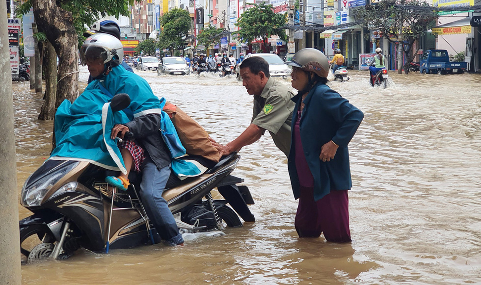A man helps another man taking his child to school push his scooter through a flooded street to school in Can Tho City, Vietnam, October 19, 2020. Photo: Chi Cong / Tuoi Tre