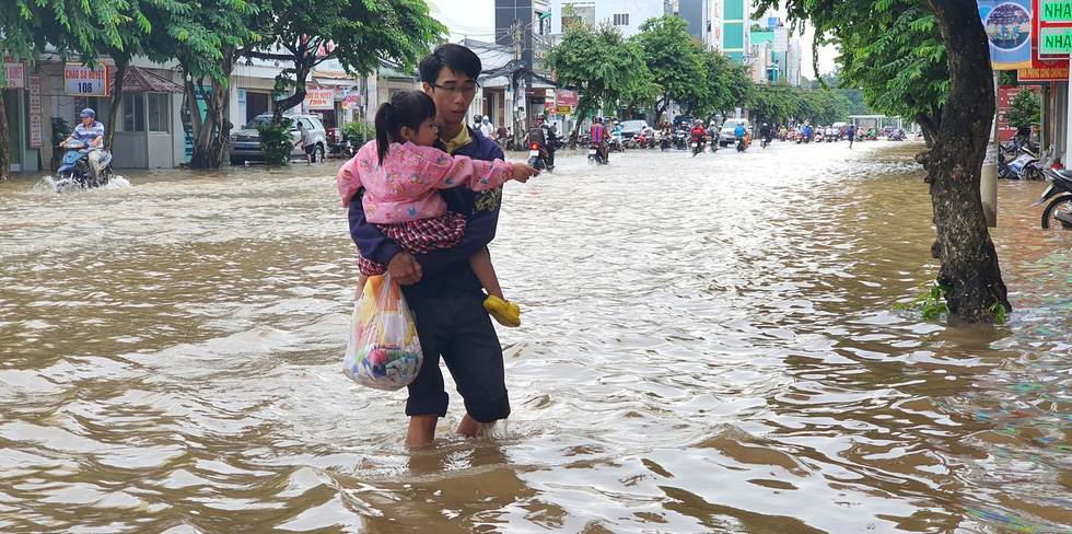 A man holding a child in his arms wades to a kindergarten in Can Tho City, Vietnam, October 19, 2020. Photo: Chi Quoc / Tuoi Tre