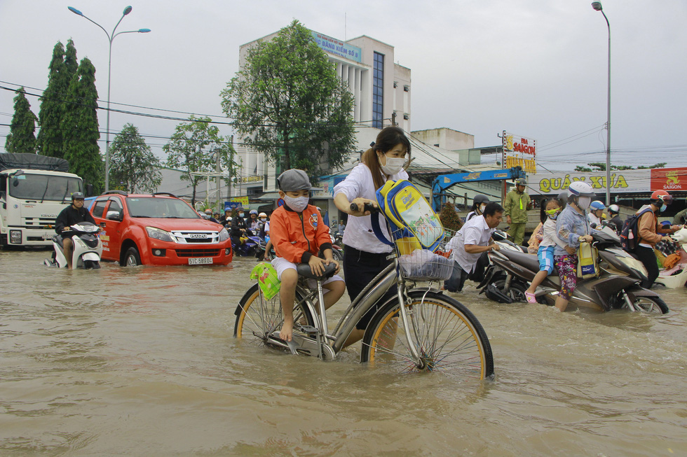 A woman walks a bicycle carrying her son through a flooded street to school in Can Tho City, Vietnam, October 19, 2020. Photo: Chi Cong / Tuoi Tre