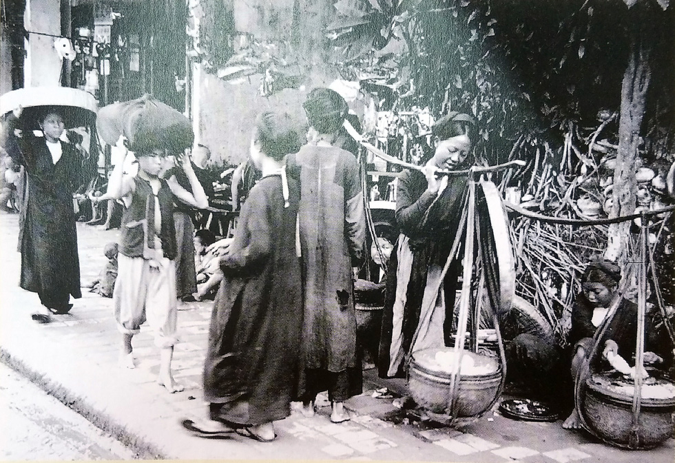 A photo depicts a street and passers-by in Hanoi, Vietnam prior to 1922.