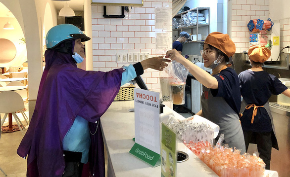 44-year-old Le Ngoc Lan (L) picks up two glasses of bubble milk tea from a shop in Binh Thanh District before delivering them to a client in District 2 in Ho Chi Minh City, Vietnam. Photo: Dieu Qui/ Tuoi Tre.