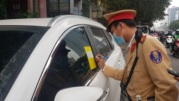 A traffic police officer fills in a parking ticket stuck on a windshield of a car on a street in Hanoi on December 14, 2020. Photo: Quang Hieu