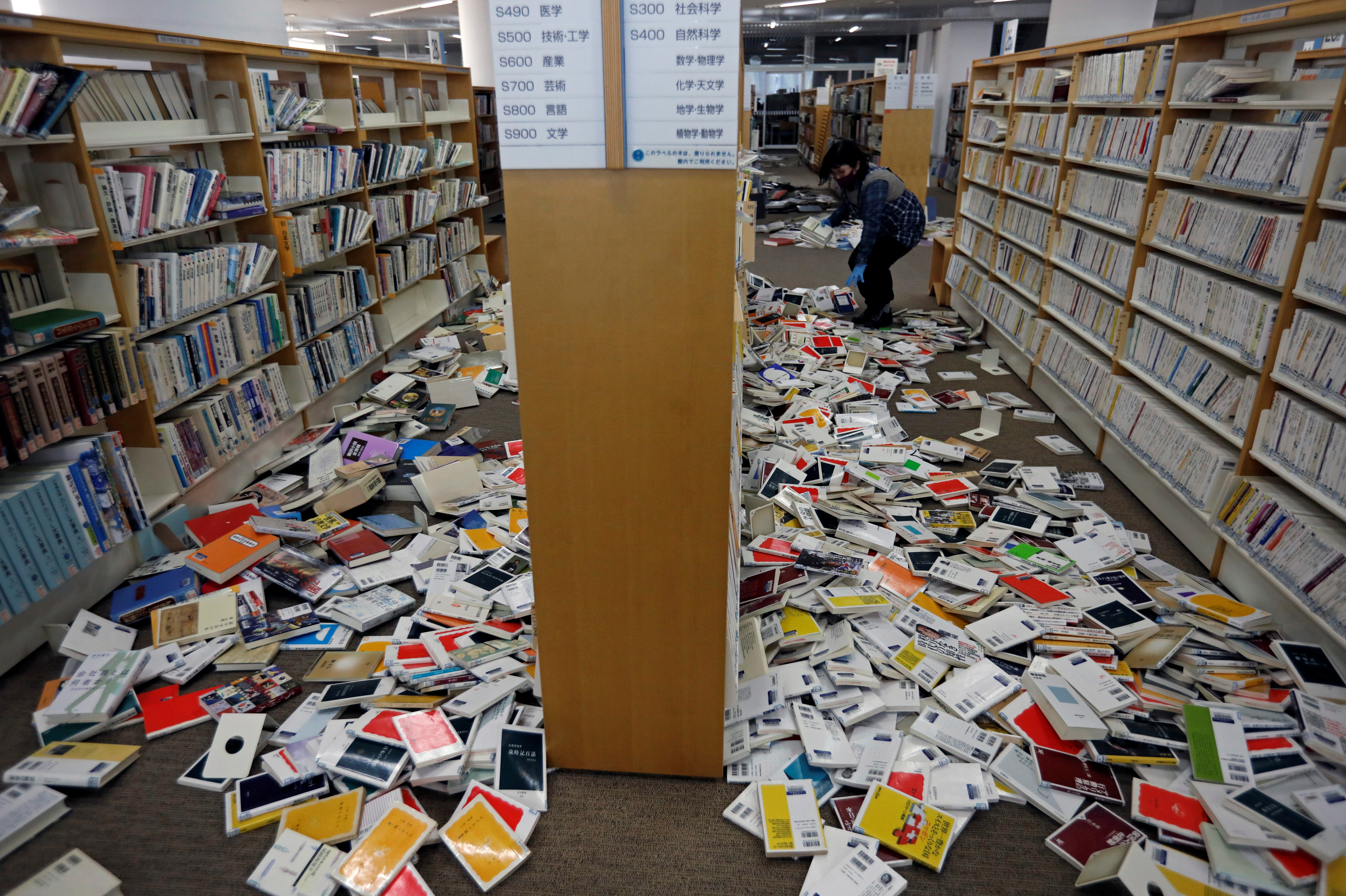 A staff member of library tries to restore books after they fell from book shelves by a strong earthquake at Iwaki City library in Iwaki, Fukushima prefecture, Japan February 14, 2021. Photo: Reuters