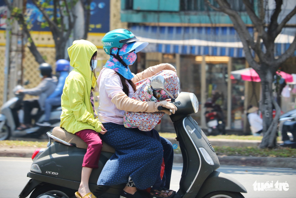 A woman carries two kids on a scooter, covered in thick clothing to avoid sunlight, in Ho Chi Minh City. Photo: Nhat Thinh / Tuoi Tre