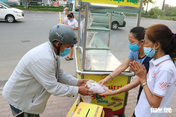 A needy worker gets a free sandwhich in from two members of the Phat Tam club. Photo: Hoang An / Tuoi Tre