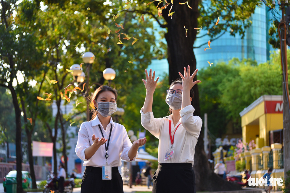 Two women throw cho nau (Dipterocarpus retusus) seeds and watch them float down in downtown Ho Chi Minh City. Photo: Ngoc Phuong / Tuoi Tre