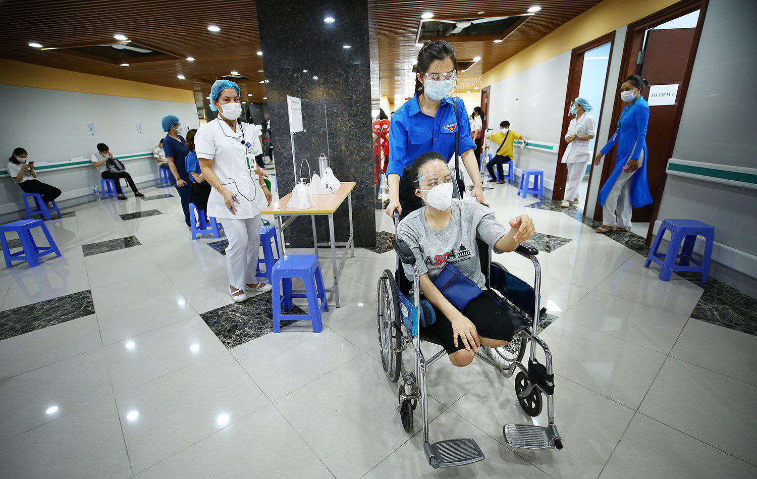 A volunteer moves a disabled worker on a wheel chair to a COVID-19 vaccination room in Hanoi, July 29, 2021. Photo: Ministry of Planning and Investment