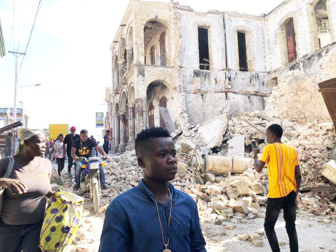 People walk along the street next to destroyed buildings following an earthquake in Jeremie, Haiti August 14, 2021, in this picture obtained from social media. Courtesy of Twitter @JCOMHaiti/ via Reuters