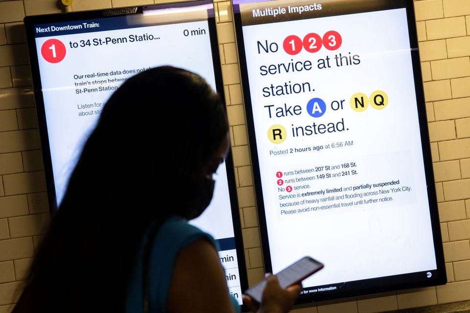 A commuter checks her phone with signs warning of delays caused by heavy rainfall and flooding in the New York City subway after the remnants of Tropical Storm Ida brought drenching rain and the threat of flash floods to parts of the northern mid-Atlantic, in New York City, U.S., September 2, 2021. Photo: Reuters