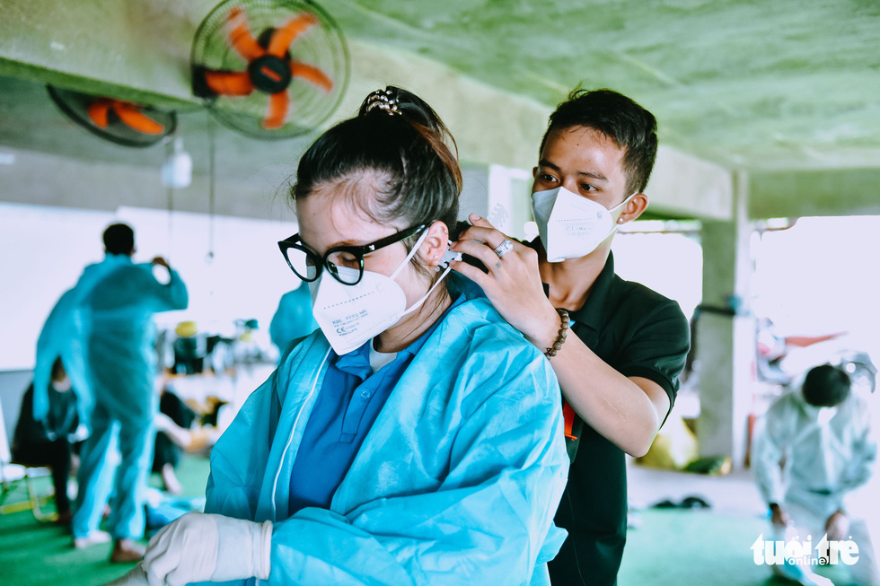 Another team member helps Cao Thi Thanh Thao to wear ear covers to prevent being hurt while spraying disinfectant. Photo: Ngoc Phuong / Tuoi Tre
