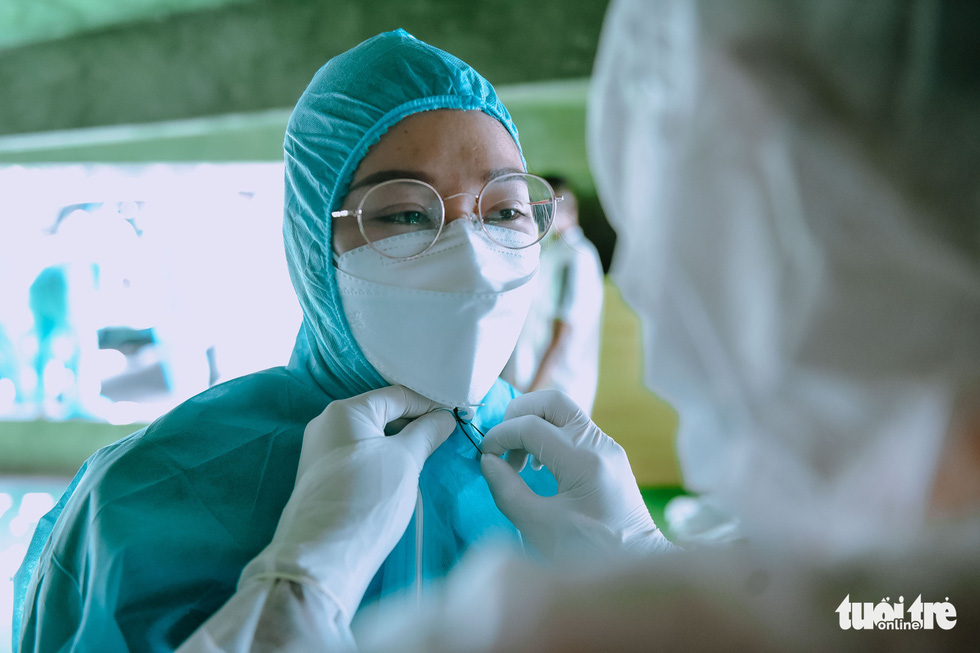 Another team member helps Luu Thi My Lil to fasten some strings as the personal protective equipment is too large for her. Photo: Ngoc Phuong / Tuoi Tre