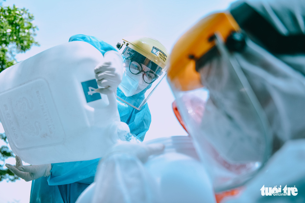 Cao Thi Thanh Thao pours disinfectant into another team member’s container. Photo: Ngoc Phuong / Tuoi Tre