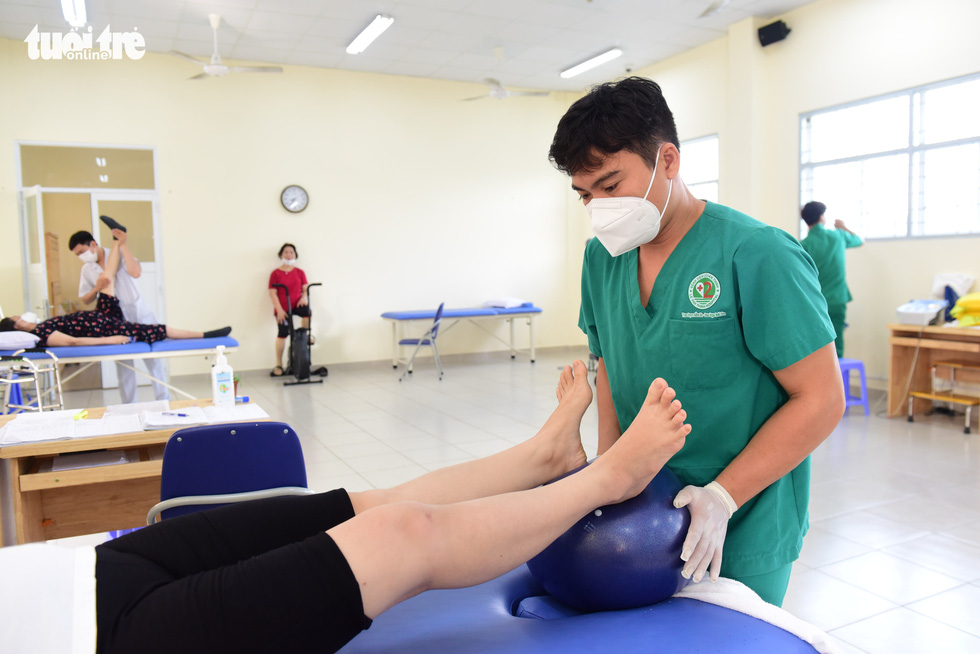 A health worker is seen instructing a former COVID-19 patient to practice a therapy with a ball at Le Van Thinh Hospital.