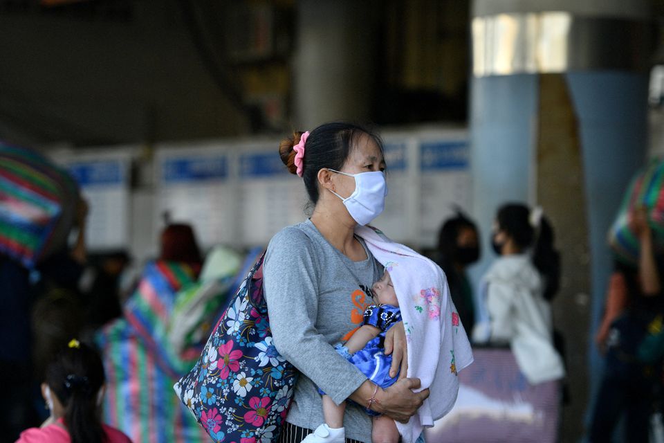 A woman wearing a mask carries a baby at a bus station after many workers crowded the terminal station to return to their cities after many activities have been closed due to coronavirus disease (COVID-19) outbreak, in Bangkok, Thailand March 22, 2020. Photo: Reuters