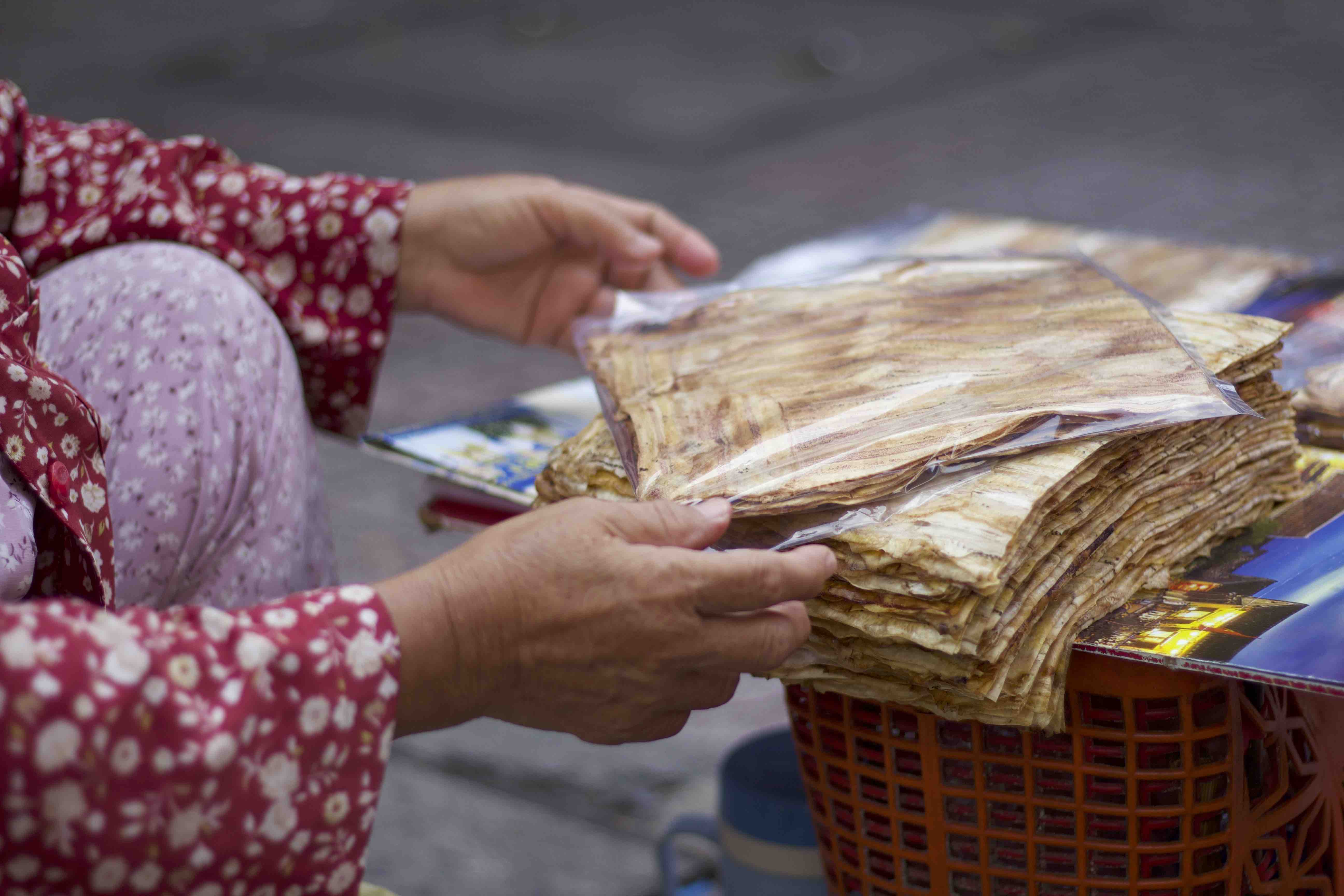 Nguyen Thi Loi packages banh chuoi nuong in a plastic bag for customers after grilling the snacks. Photo: Linh To / Tuoi Tre