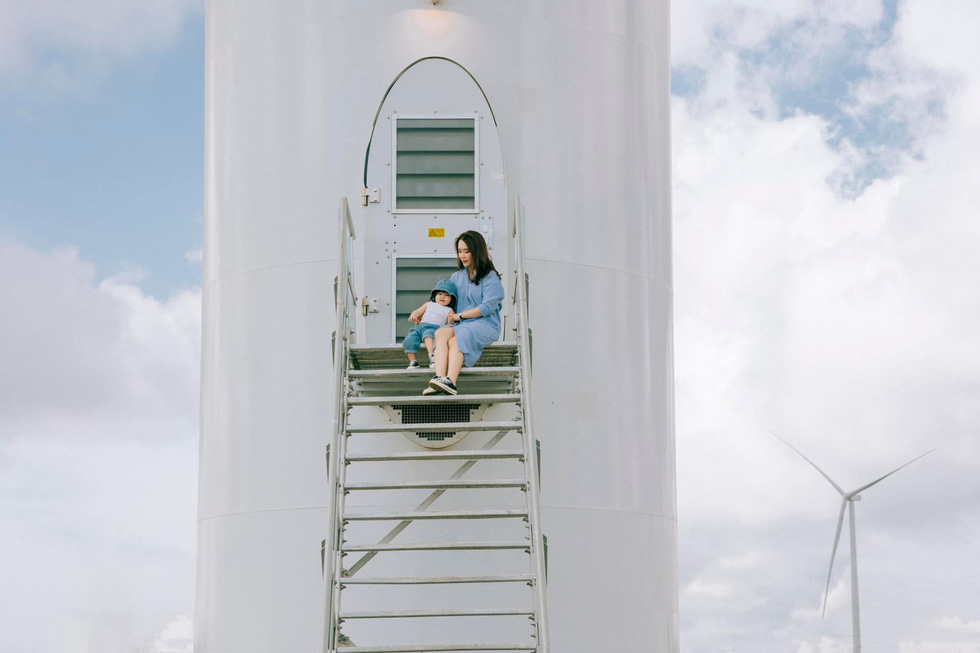 A child and her mom pose for a photo in front of a wind turbine background at Cau Dat Tea Farm in Da Lat City's Xuan Truong Commune. Photo: Nguyen Hien / Tuoi Tre