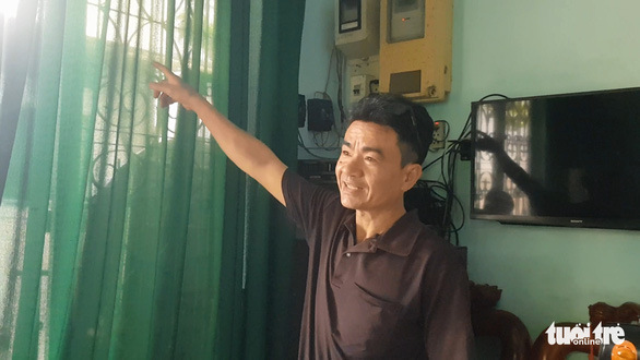 This image shows Dang Van Ka pointing his hand to the door curtains where the clouded monitor clung on after straying into his home in early June 2022. Photo: Ngoc Khai / Tuoi Tre