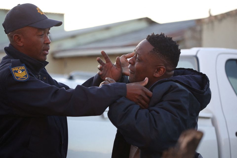 A family member reacts next to a police officer as forensic personnel investigate after the deaths of patrons found inside the Enyobeni Tavern, in Scenery Park, outside East London in the Eastern Cape province, South Africa, June 26, 2022. Photo: Reuters
