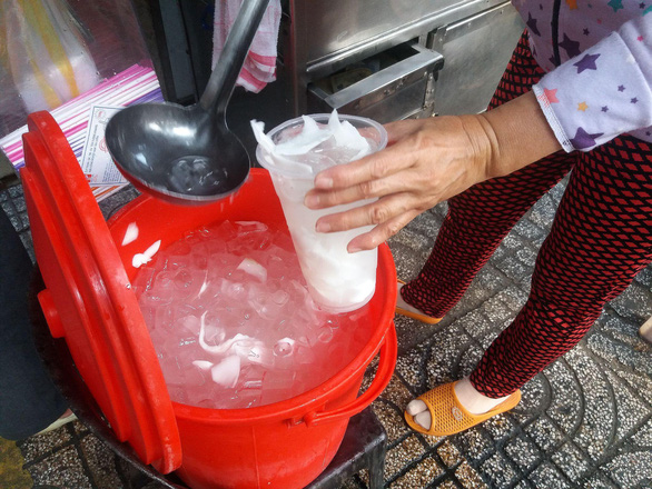 A woman scoops coconut water into a plastic cup for customers at the stall in front of 250 Pasteur Street in District 3, Ho Chi Minh City. Photo: Minh Duc / Tuoi Tre