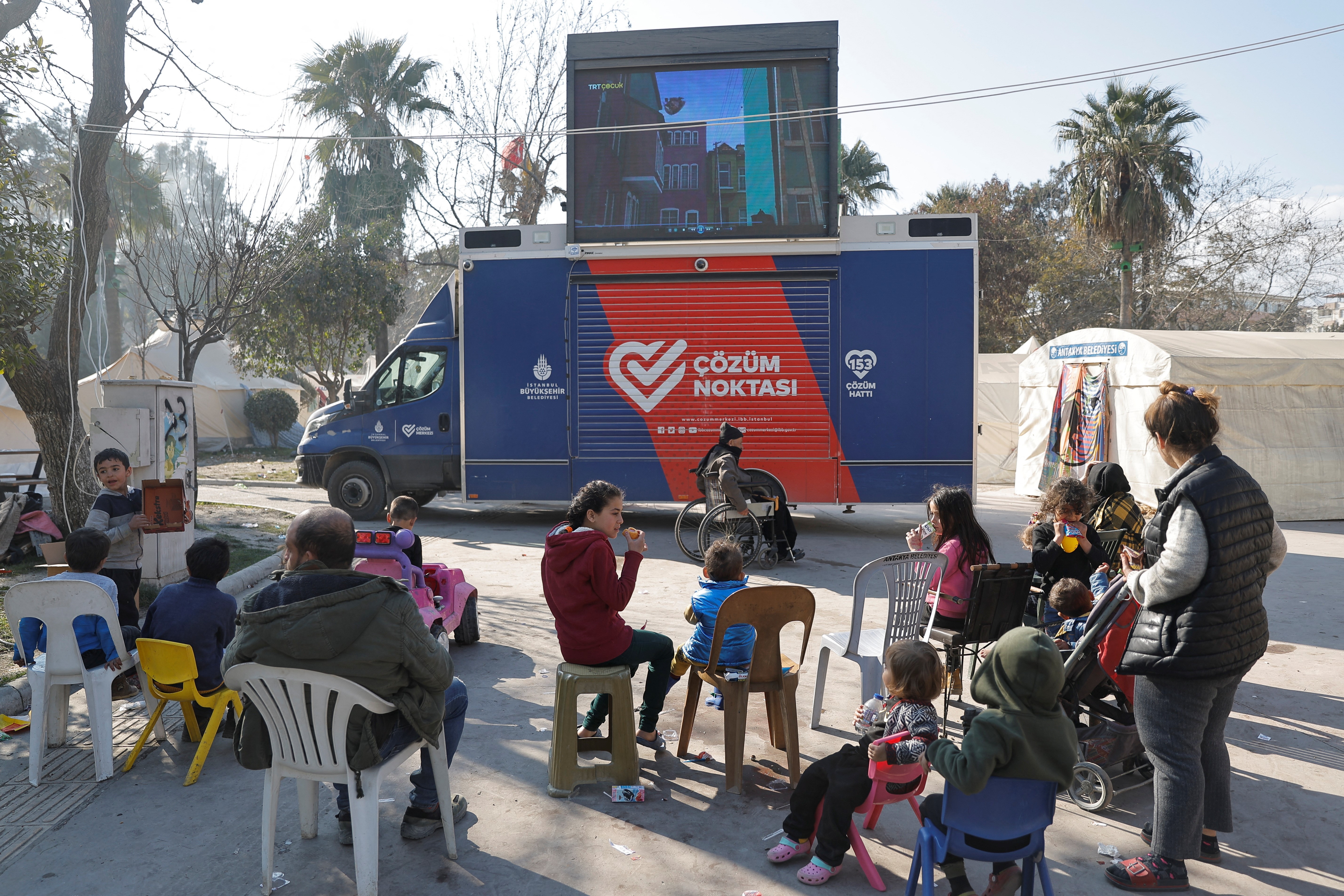 People watch cartoons on a screen at a camp, in the aftermath of the deadly earthquake, in Antakya, Turkey February 18, 2023. Photo: Reuters