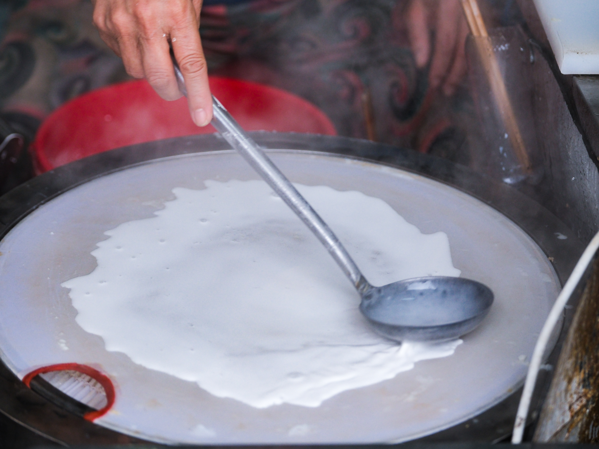 Dinh Thi Tam spreads rice batter on top of a steamer to make banh cuon at her Banh Cuon Cao Bang stall in Hanoi, Vietnam. Photo: Nam Tran / Tuoi Tre News