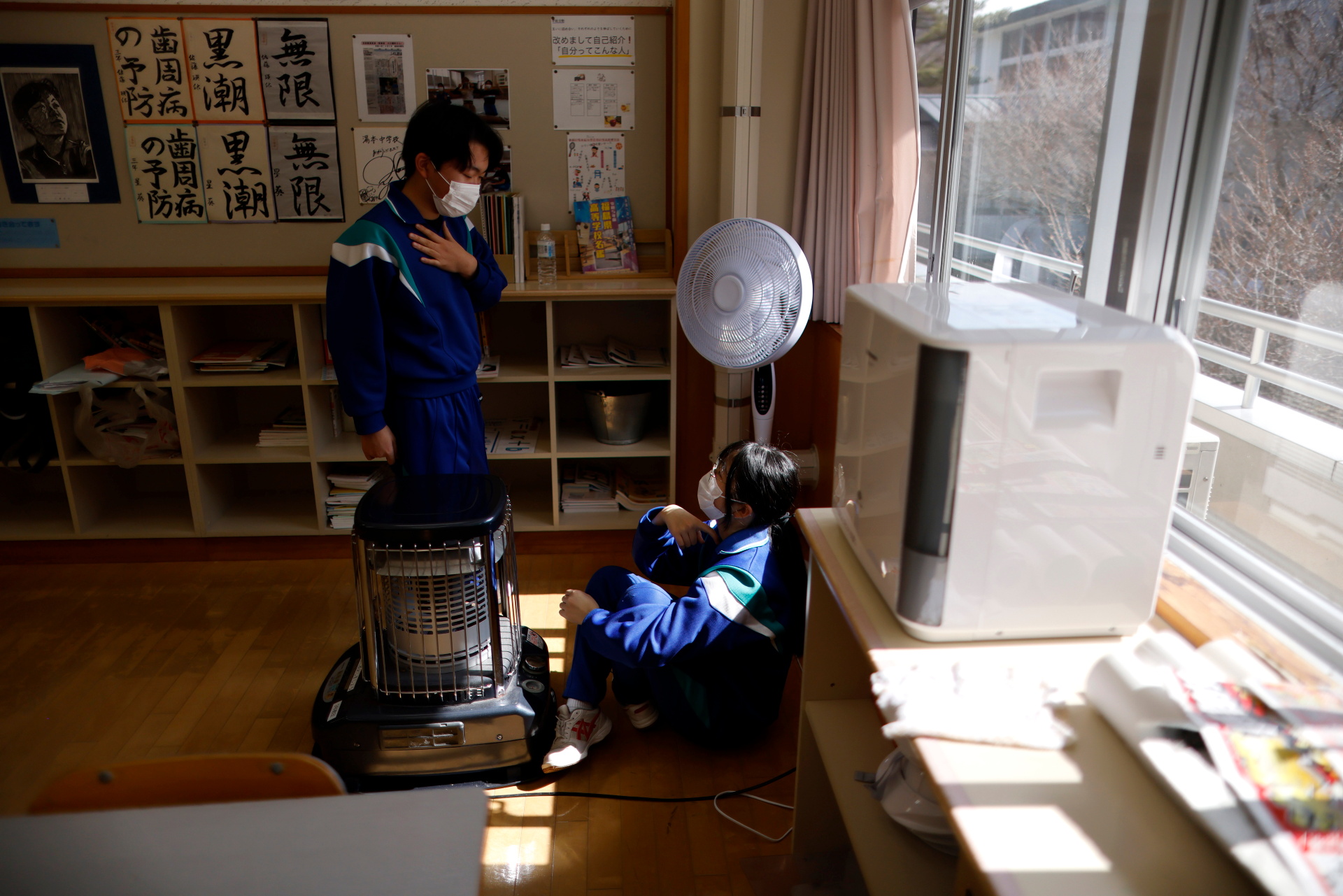 Eita and Aoi keep warm next to a stove during break time between lessons, a day before graduation and the school’s closing ceremony, in Ten-ei Village, Fukushima Prefecture, Japan, March 10, 2023. Photo: Reuters