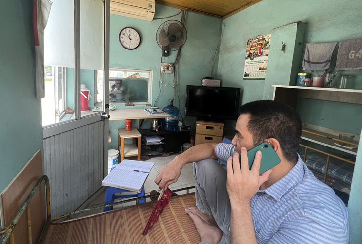 A security guard of a company in Hoai Duc District, Hanoi works in a narrow room. He must use a paper fan during the power cut. Photo: Pham Tuan / Tuoi Tre