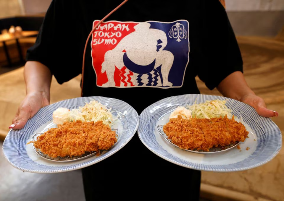 An employee of Yokozuna Tonkatsu Dosukoi Tanaka, a sumo wrestling themed restaurant, serves Tonkatsu or breaded pork cutlets to tourists from abroad, in Tokyo, Japan June 30, 2023. Photo: Reuters