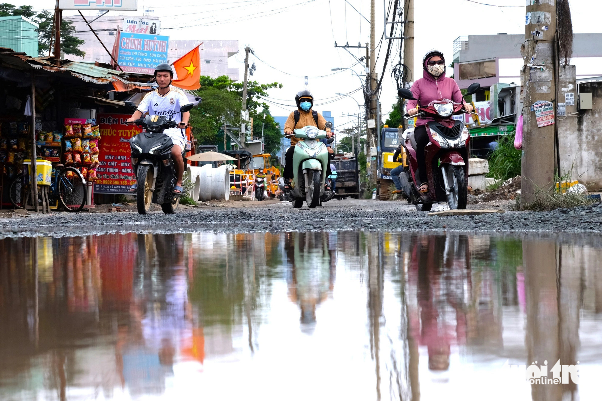 A large waterlogged pothole is seen in front of motorcyclists. Photo: Phuong Nhi / Tuoi Tre