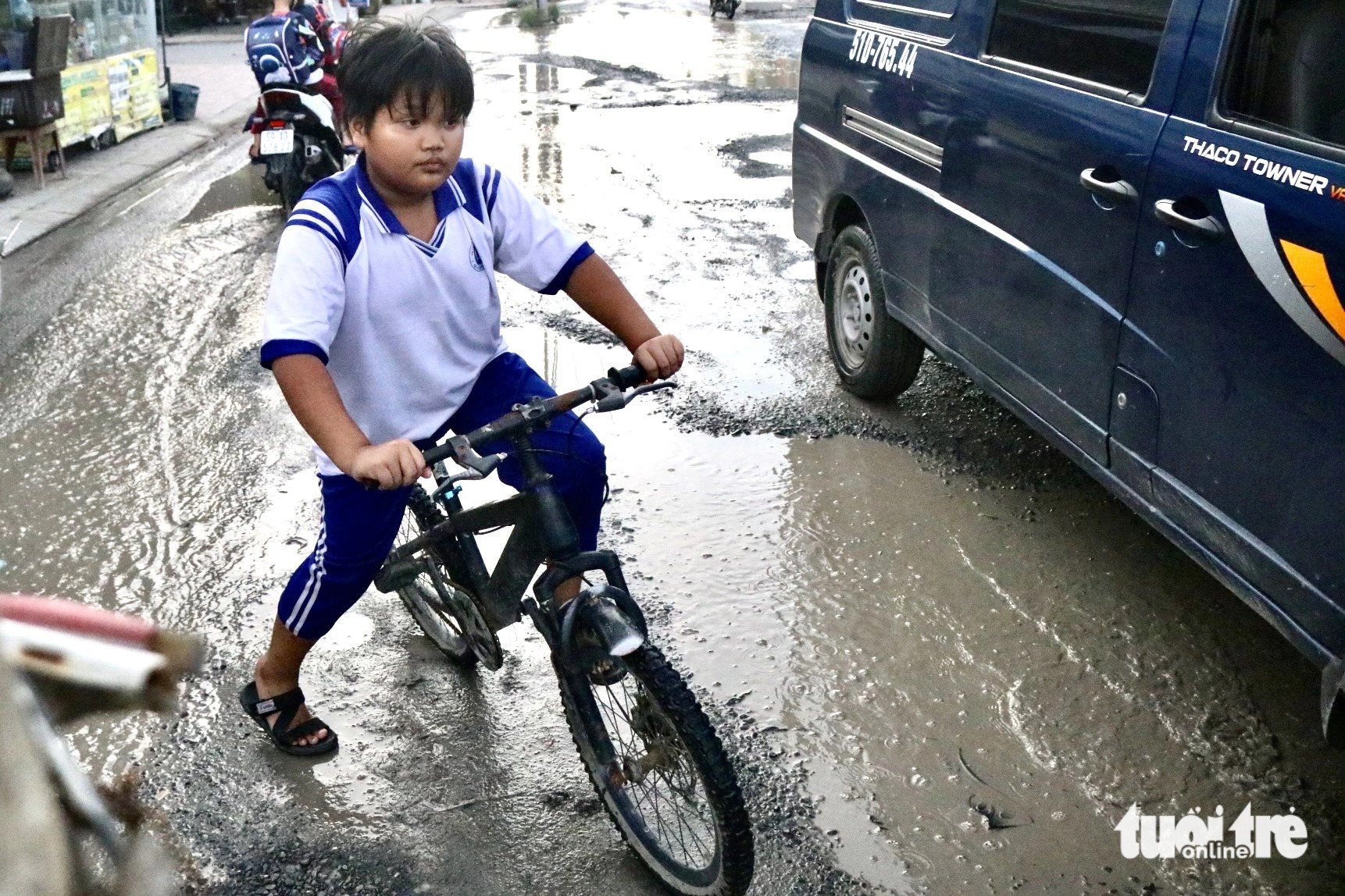 Students who cycle like this schoolboy could get their clothes and shoes splashed with mud when passing by this muddy, potholed road. Photo: Tien Quoc / Tuoi Tre