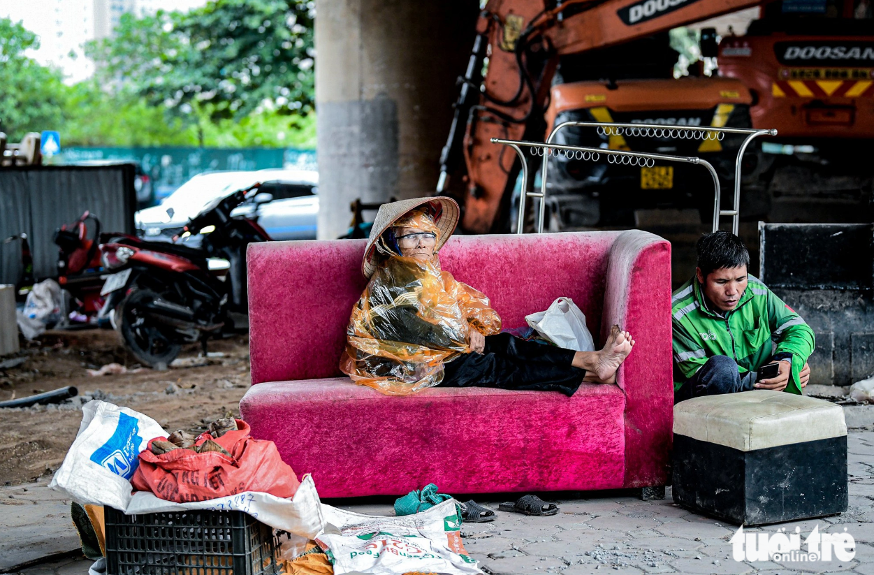An elderly vendor of banh gai (gai leaf cake) huddles in the chilly wind under Me Tri Bridge, wearing a raincoat to shield herself from the cold. Photo: Nam Tran / Tuoi Tre