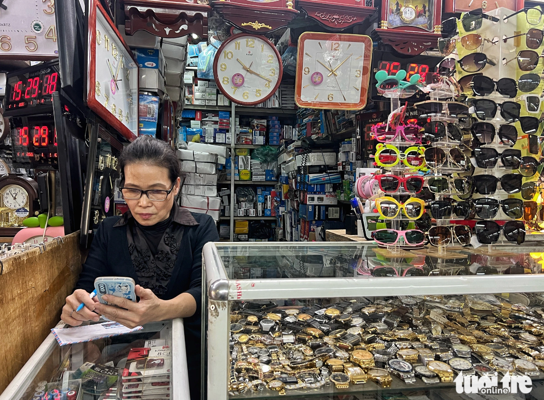 Hang, a vendor at a stall of watches and glasses at Dong Xuan Market, is pictured surfing the Internet due to no buyers. Photo: Pham Tuan / Tuoi Tre