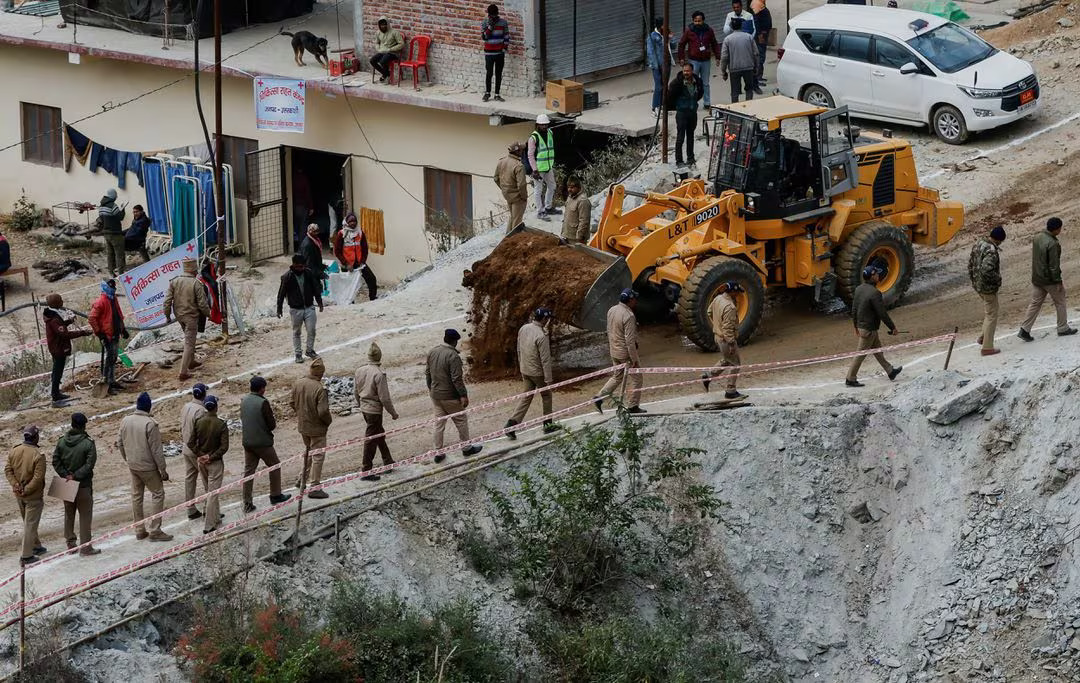 Policemen walk past a bulldozer as it lays down mud to flatten a road outside the tunnel where operations are underway to rescue trapped workers, after a tunnel collapsed in Uttarkashi in the northern state of Uttarakhand, India, November 28, 2023. Photo: Reuters