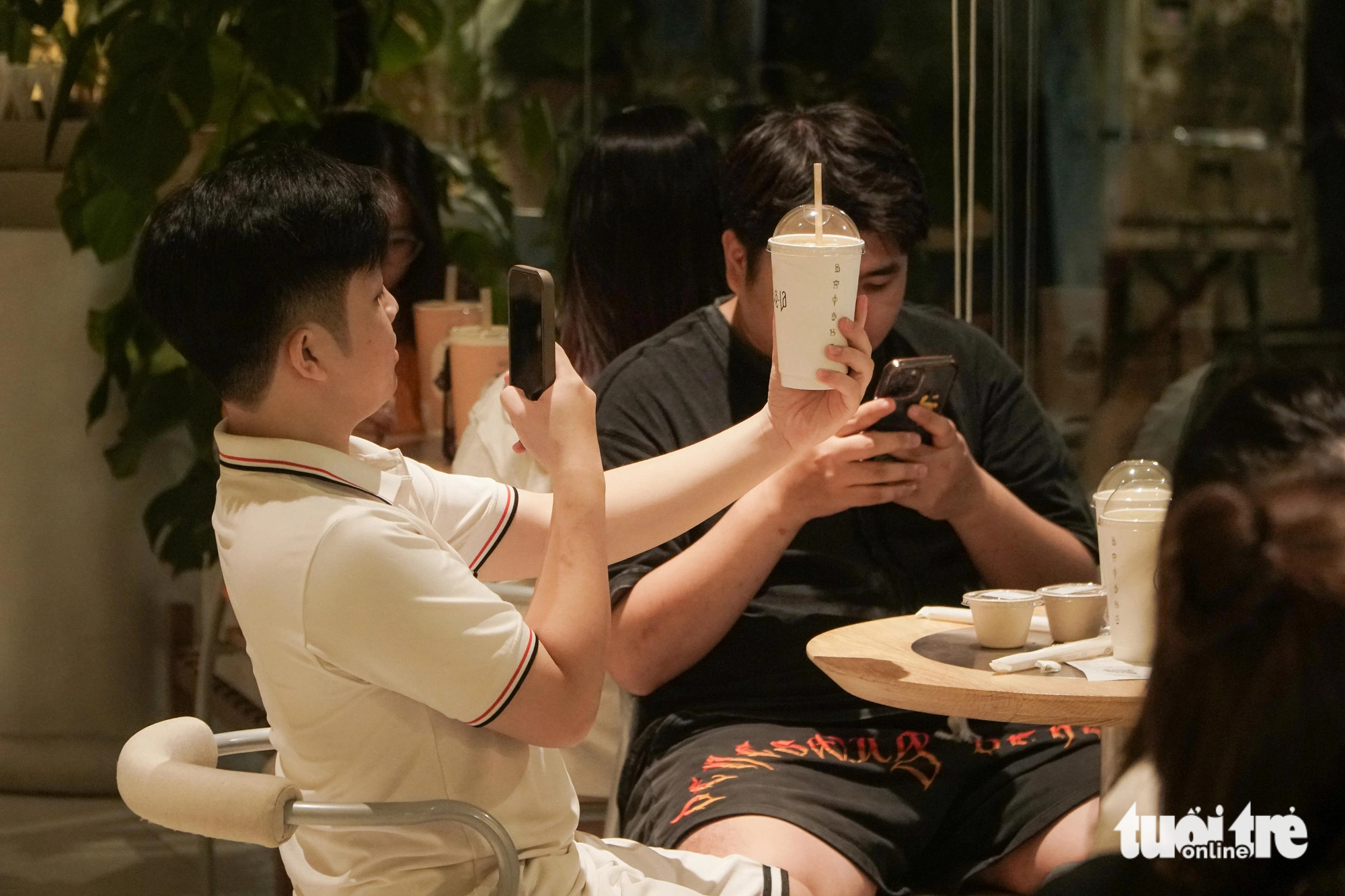 A customer takes a photo of his cup of beverage at a coffee shop on Tong Dan Street in Hoan Kiem District, Hanoi, at dawn on June 14, 2024. Photo: Pham Tuan / Tuoi Tre