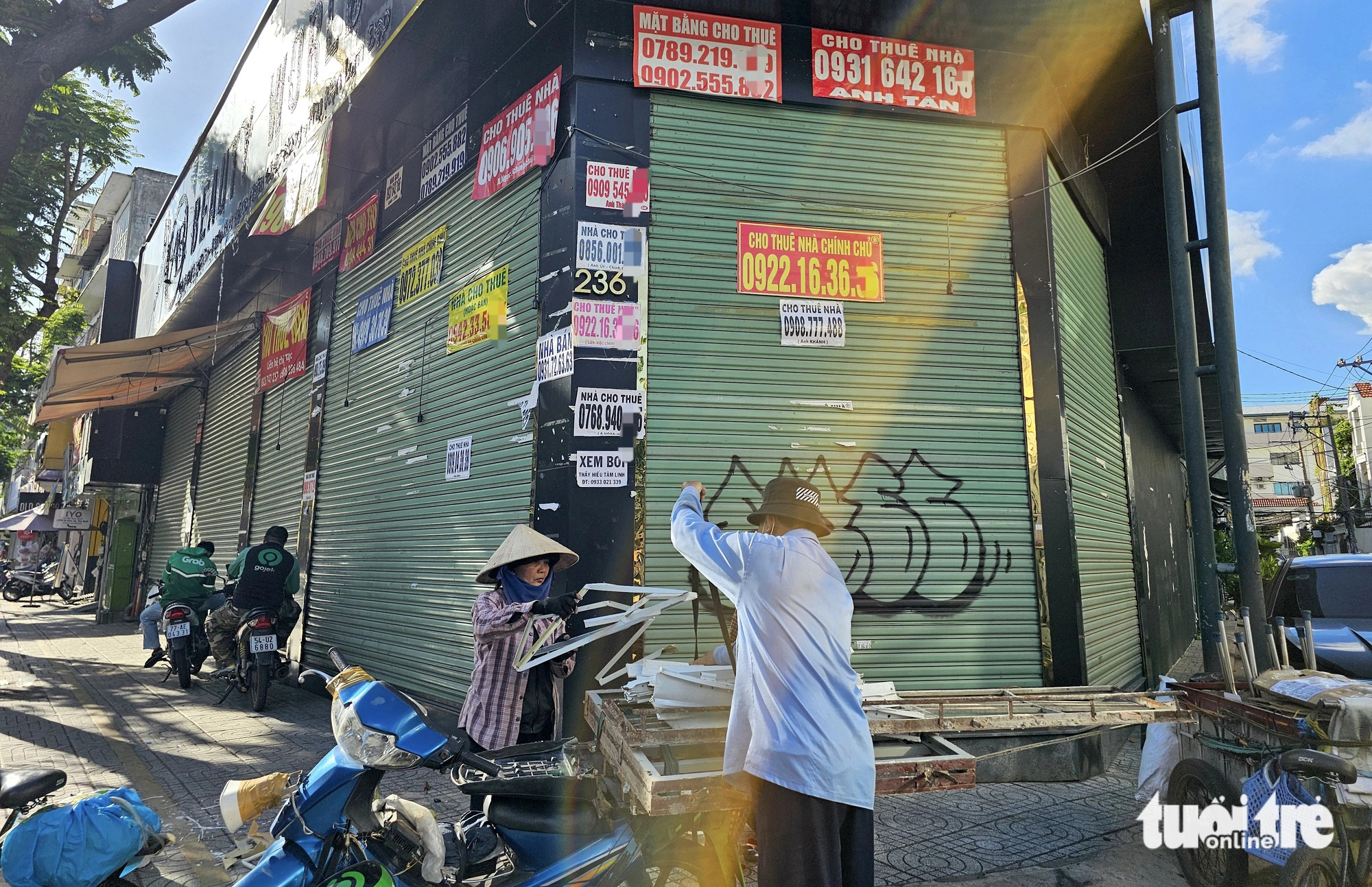 A closed supermarket on a street corner has it front side and surrounding sidewalk transformed into a gathering place for scrap dealers, as well as a spot for motorbike taxi drivers to take their lunch breaks in downtown Ho Chi Minh City. Photo: Ngoc Hien / Tuoi Tre