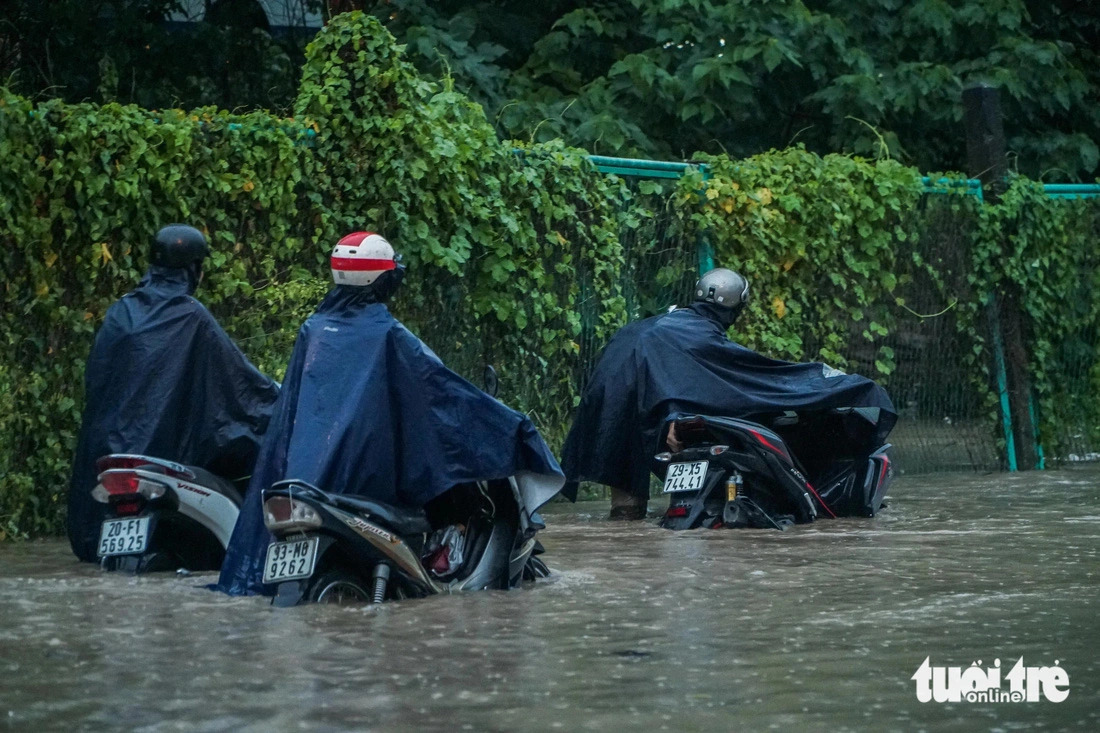 Many people have to walk to take their broken-down motorbikes out of a seriously flooded area in Hanoi in the heavy rain on July 23, 2024. Photo: Pham Tuan / Tuoi Tre