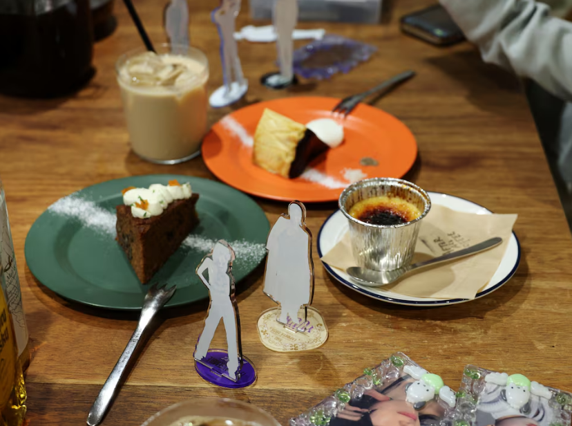 Momoka Matsui and her co-worker Saki Matsumoto prepare to take photos of acrylic stand figure models of their favorite idols with cakes and teas, which they ordered at After All Coffee, where Matsui’s favorite boy band stopped by, in Tokyo, Japan March 23, 2025. Photo: Reuters
