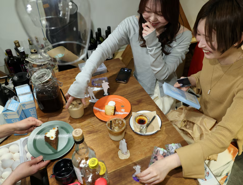 Momoka Matsui and her co-worker Saki Matsumoto prepare to take photos of acrylic stand figure models of their favorite idols with cakes and teas, which they ordered at After All Coffee, where Matsui’s favorite boy band stopped by, in Tokyo, Japan March 23, 2025. Photo: Reuters