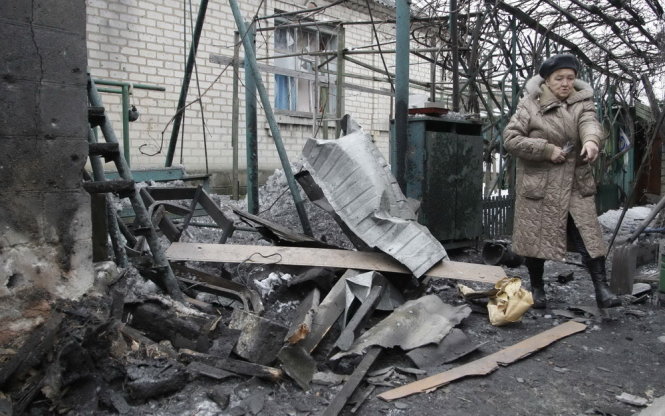 Một phụ nữ đứng trước căn nhà đổ nát do đạn pháo tại Donetsk, miền đông Ukraine - Ảnh: Reuters