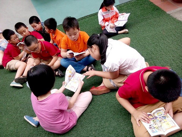 Các em học sinh trường tiểu học Lomonoxop Mỹ Đình ngồi bệt trên cỏ đọc sách - Ảnh: Trường Lomonoxop