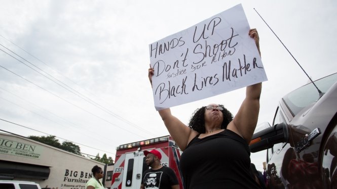 Người biểu tình giơ cao biểu ngữ trước Dinh Thống đốc bang Minnesota sau sự việc - Ảnh: Reuters