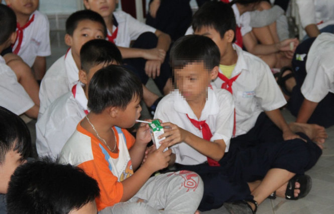 Các em học sinh lấy sữa của mình rồi tự tay mở ống hút, găm vào hộp sữa để mời các bạn nạn nhân chất độc da cam - Ảnh: ĐOÀN CƯỜNG