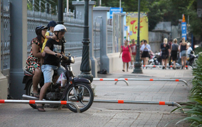 Người đàn ông chở phụ nữ và trẻ nhỏ đang cố luồn lách qua các  thanh Barie trên đường Lý Tự Trọng (Q.1) - Ảnh: LÊ PHAN