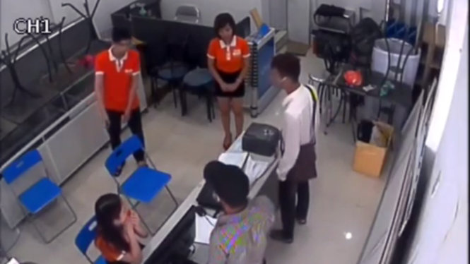 Hai nghi phạm (áo trắng và áo kẻ xám) khống chế các nhân viên bán hàng - Ảnh cắt từ clip