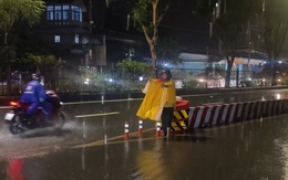 Ông Nguyễn Đắc Lắc mặc áo mưa lội nước, hướng dẫn xe qua đoạn đường ngập ở TP.HCM